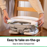 Ingenuity Deluxe Comfort folding grey baby booster seat with adjustable tray and harness on dining chair