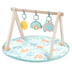 Ingenuity Sun Valley Wooden Toy Arch with foldable A-frame, attached plush rainbow, elephant, and sunshine mirror toys on a neutral-colored baby play mat for ages 0-36 months