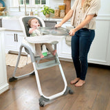 Baby in a high chair with a woman holding a tray in a kitchen.