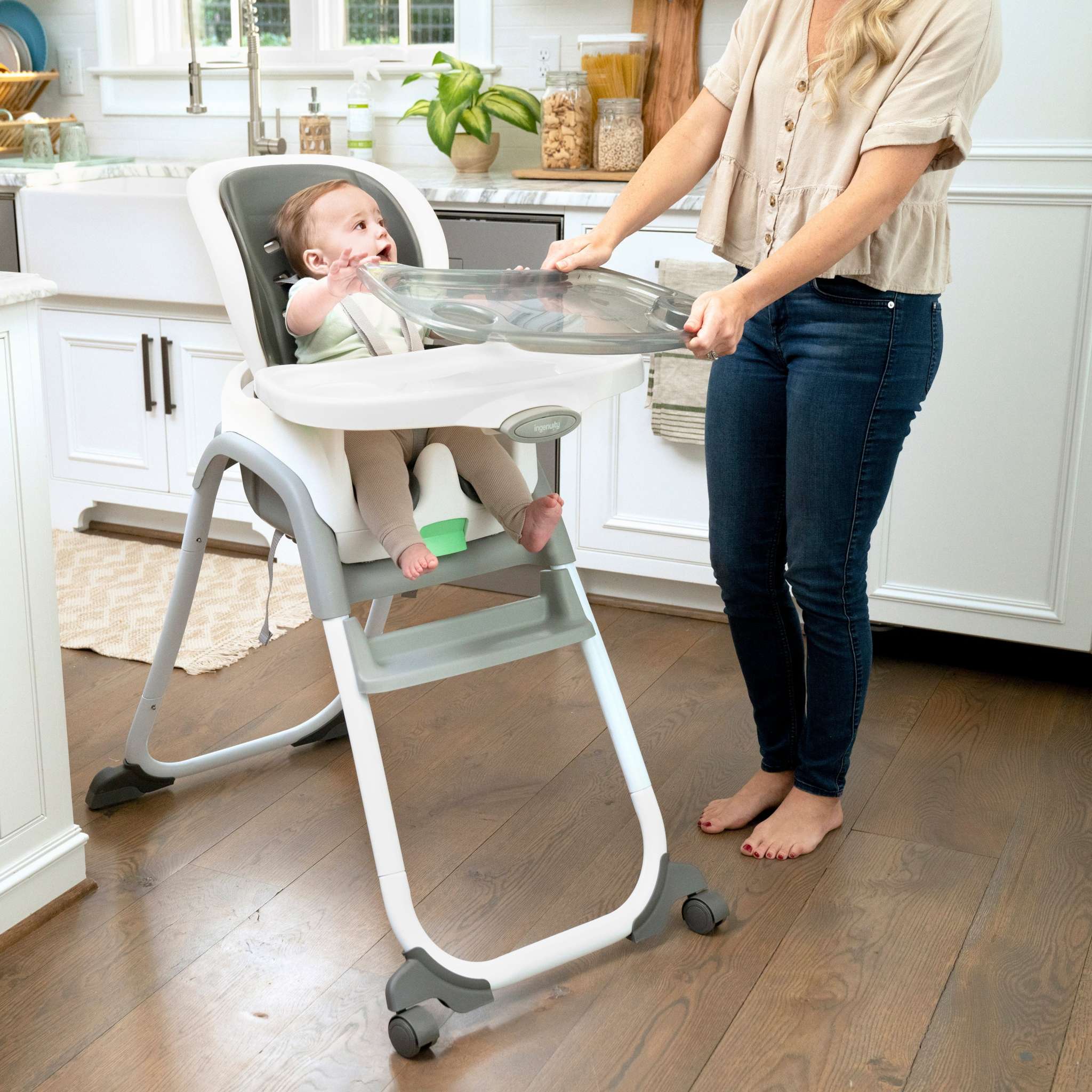 Baby in a high chair with a woman holding a tray in a kitchen.