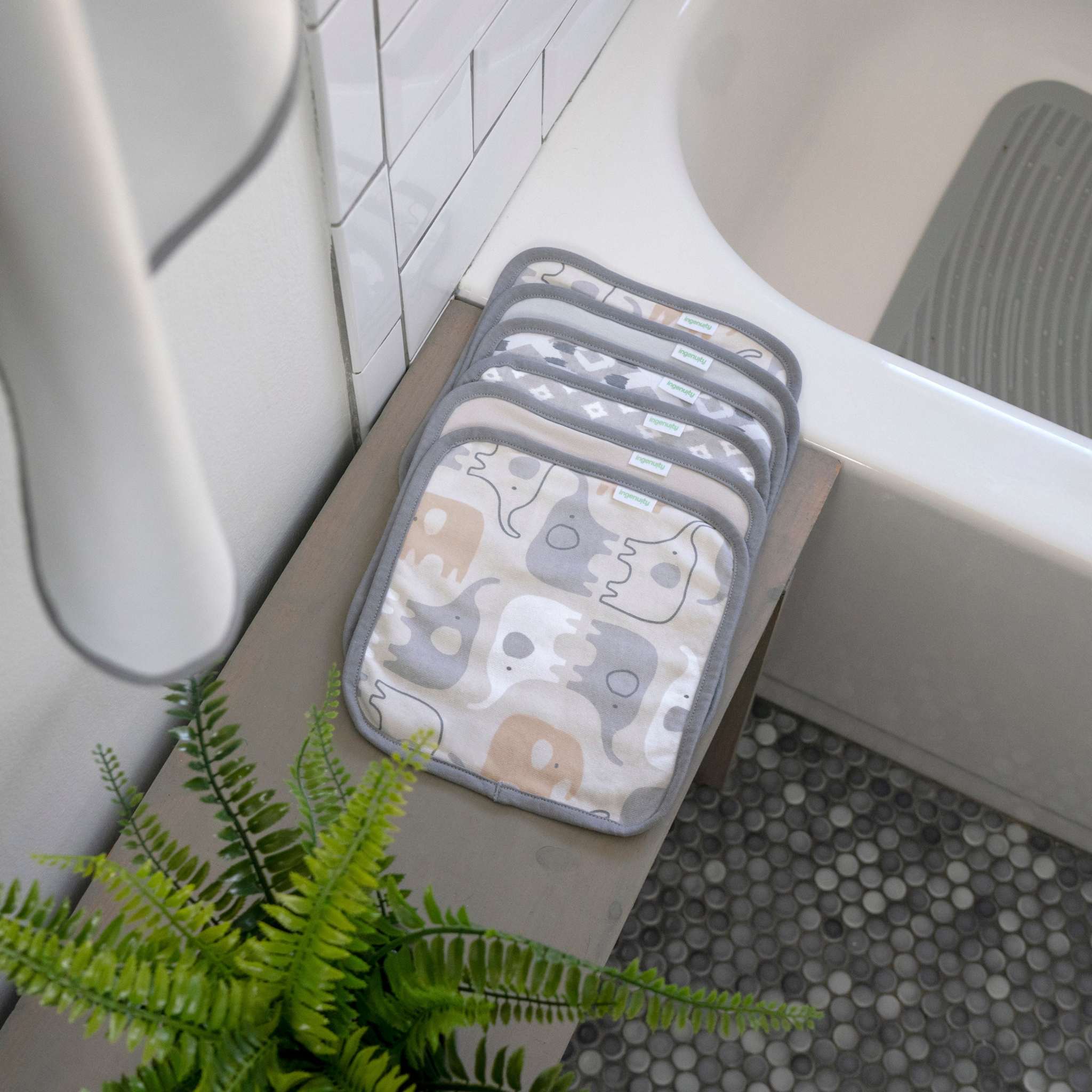Set of bath mats with elephant pattern on a bathtub ledge next to a plant.