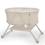Ingenuity Snooze & Stow™ easy-folding bassinet with sound, light, vibration, mesh sides, and storage shelf in sand color.