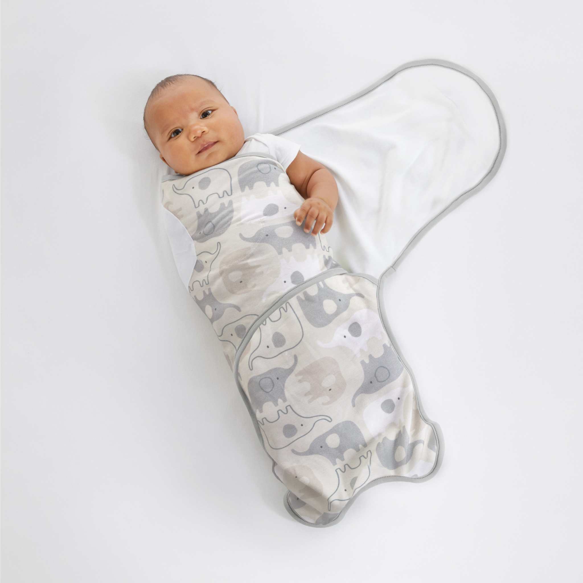 Baby wrapped in a gray elephant-patterned swaddle on a white background