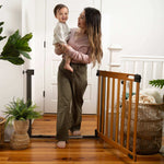 Ingenuity The Thruway 60W Series honey oak wood and metal safety gate for babies and pets installed in doorway